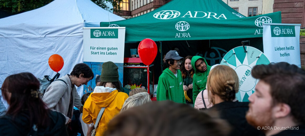 ADRA-Stand auf dem Schlossgrabenfest 2024 mit einer Drehscheibe für Gewinne, einer Popcornmaschine und grüne ADRA-Luftballons, die Besucher anziehen