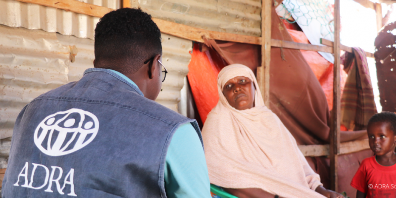 Mutter sitzt mit ihrem Kind und einem ADRA-Mitarbeiter in einer Behausung