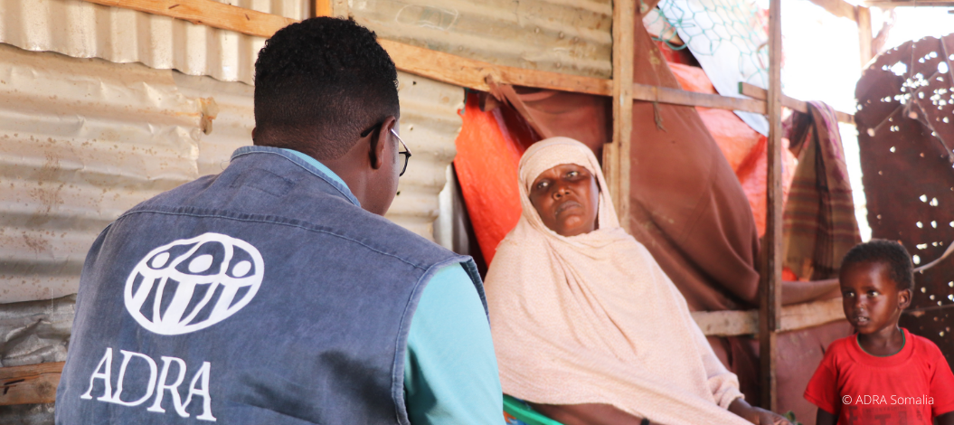 Mutter sitzt mit ihrem Kind und einem ADRA-Mitarbeiter in einer Behausung