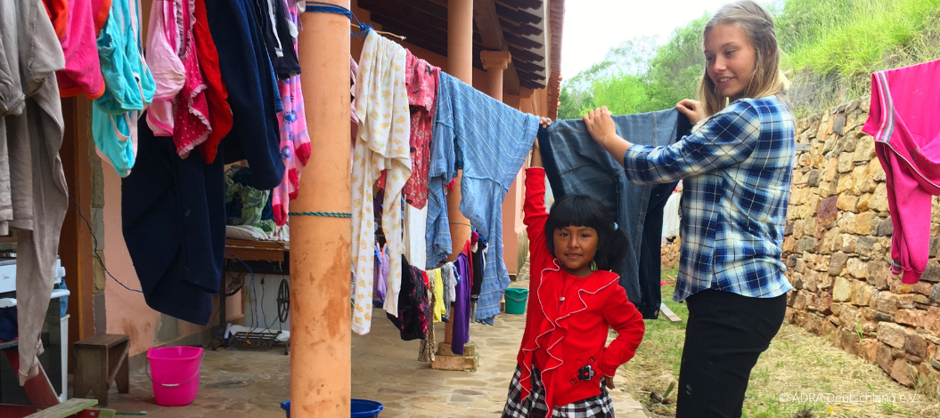 ADRAlive! Freiwillige Diana und ein hilfsbereites Mädchen hängen Wäsche zum Trocknen auf eine Wäscheleine in Bolivien