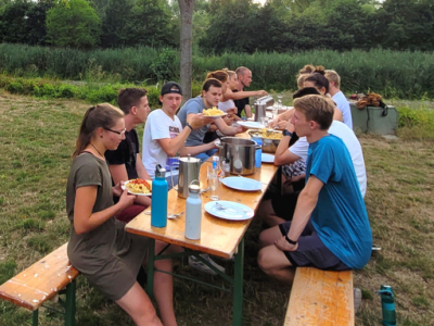 Eine Gruppe junger, glücklicher Menschen die sich im Freiwilligendienst im In- und Ausland engagieren, beim gemeinsamen Essen im Freien.