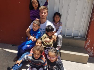 Ein Freiwilliger aus dem ADRAlive-Team sitzt zusammen mit sieben Kindern auf einer Treppenstufe und Boden und hält dabei zwei Kinder auf seinem Schoß