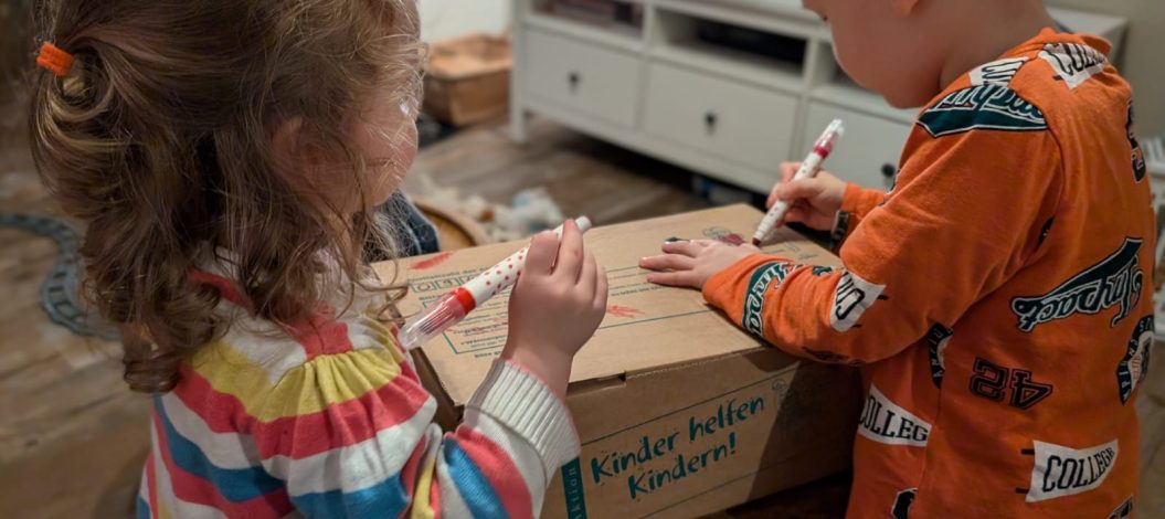 Anni (2 Jahre) und Emil (4 Jahre) verzieren das Paket, das Sie für die „Aktion Kinder helfen Kindern!“ gepackt haben. (Foto: Angela Völker)