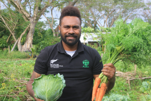 Ein lächelnder ADRA-Mitarbeiter hält Karotten und Salat in den Hände