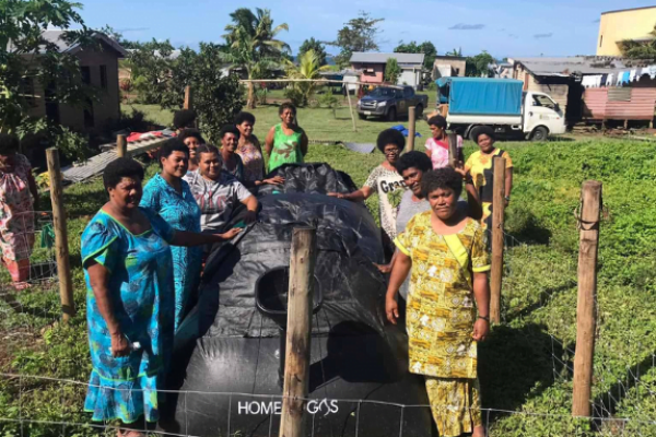 Eine Gruppe von Frauen stehen um das Biogas herum und schauen in die Kamera