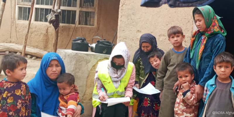 Eine ADRA-Mitarbeiterin hilft einer Gruppe von Frauen mit Kindern in Afghanistan die Formulare für Lebensmittelpakete auszufüllen