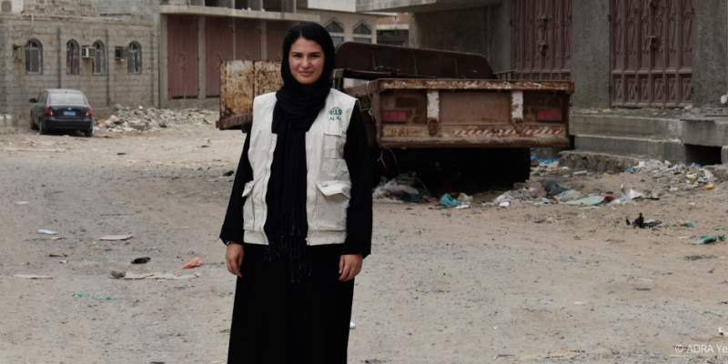 Bürgerkrieg im Jemen: Eine ADRA Mitarbeiterin steht vor den zerstörten Gebäuden, Autos und hinterlassenen Trümmern.