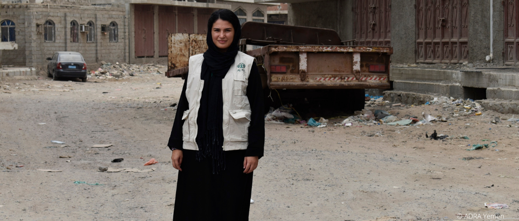 Bürgerkrieg im Jemen: Eine ADRA Mitarbeiterin steht vor den zerstörten Gebäuden, Autos und hinterlassenen Trümmern.