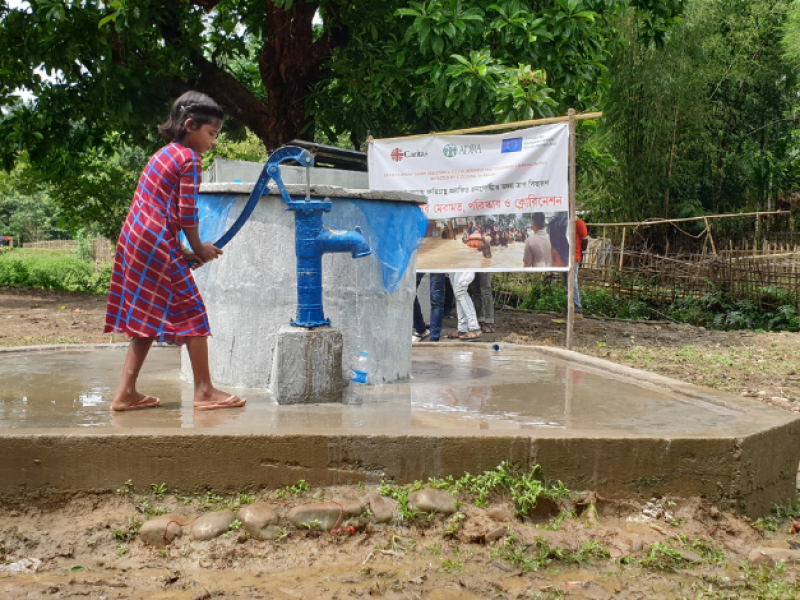 Ein junges Mädchen aus Indien steht vor einer Wasseraufbereitungsanlage und zapft sich sauberes Trinkwasser in eine Plastikflasche.