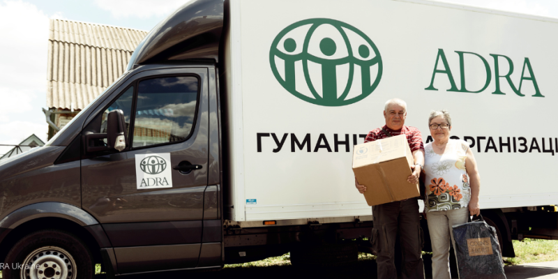 Ein Mann und eine Frau stehen vor einem ADRA-LKW in der Ukraine, welcher Hilfspakete an die Betroffenen aushändigt.