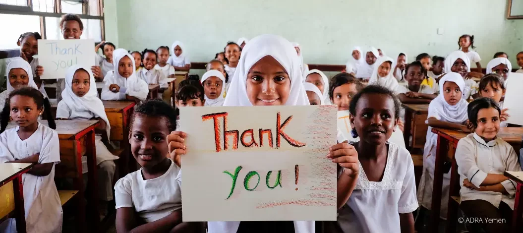 Eine Schulklasse blickt lächelnd in die Kamera und hält ein "Thank you" Schild nach oben
