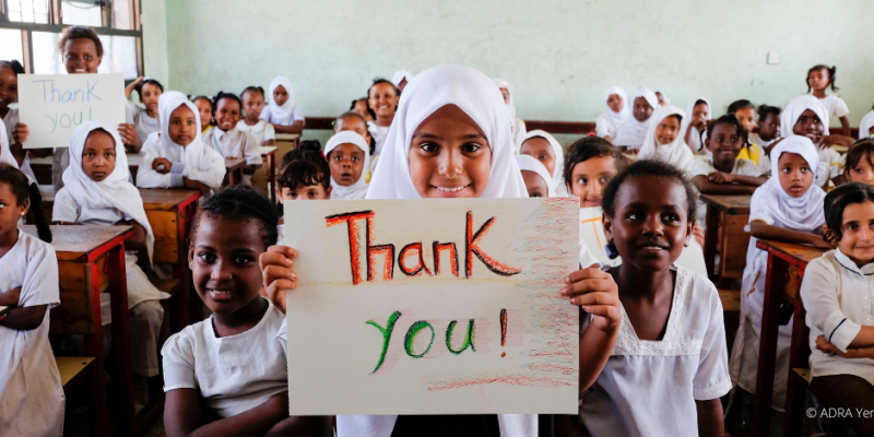 Eine Schulklasse blickt lächelnd in die Kamera und hält ein "Thank you" Schild nach oben