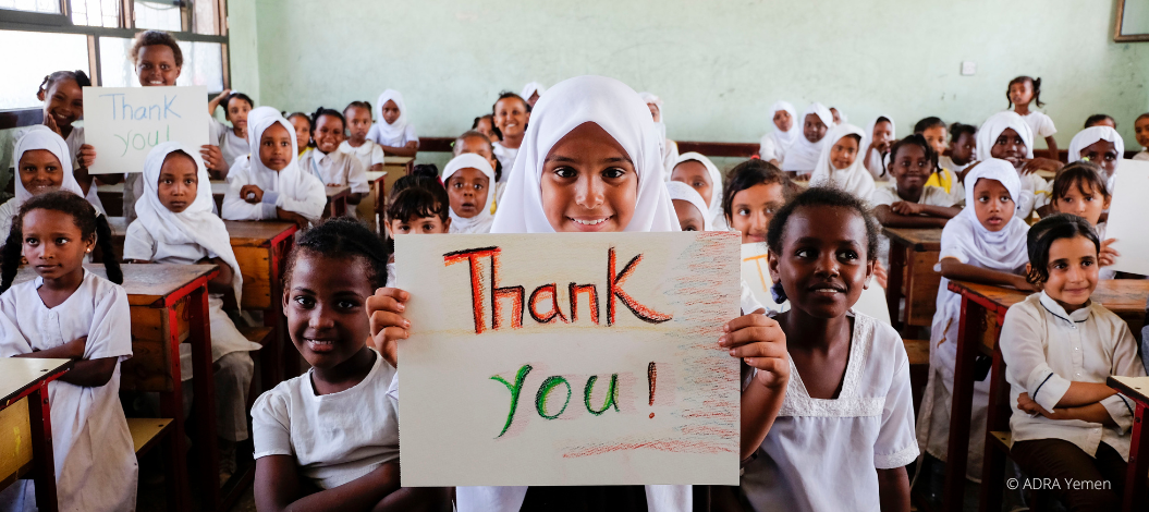 Eine Schulklasse blickt lächelnd in die Kamera und hält ein "Thank you" Schild nach oben