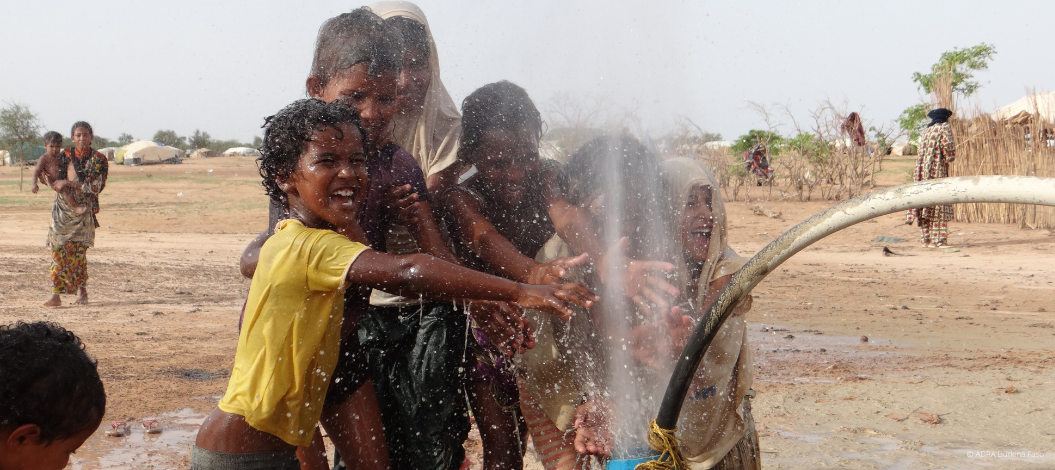 Kinder freuen sich lachend über sprudelndes Wasser aus einem Schlauch.