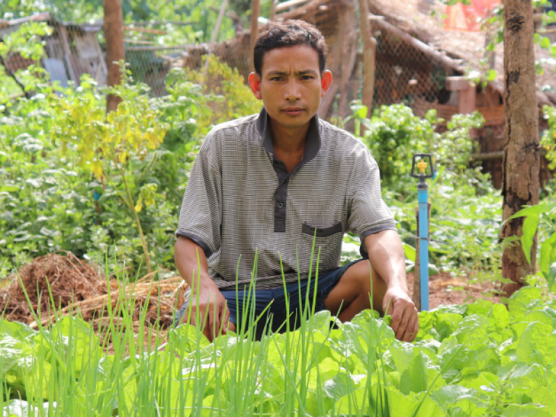 Ein Bauer aus Laos sitzt der Hocke hinter seiner Ernte.