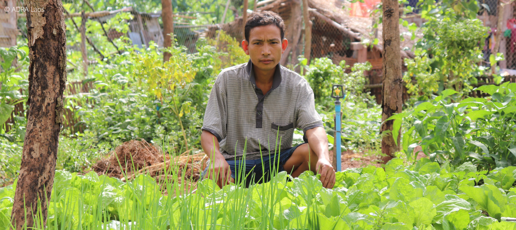 Ein Bauer aus Laos sitzt der Hocke hinter seiner Ernte.