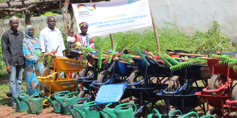 Vier Erwachsene und ein Kleinkind betrachten draußen eine Auswahl an Gartenwerkzeugen