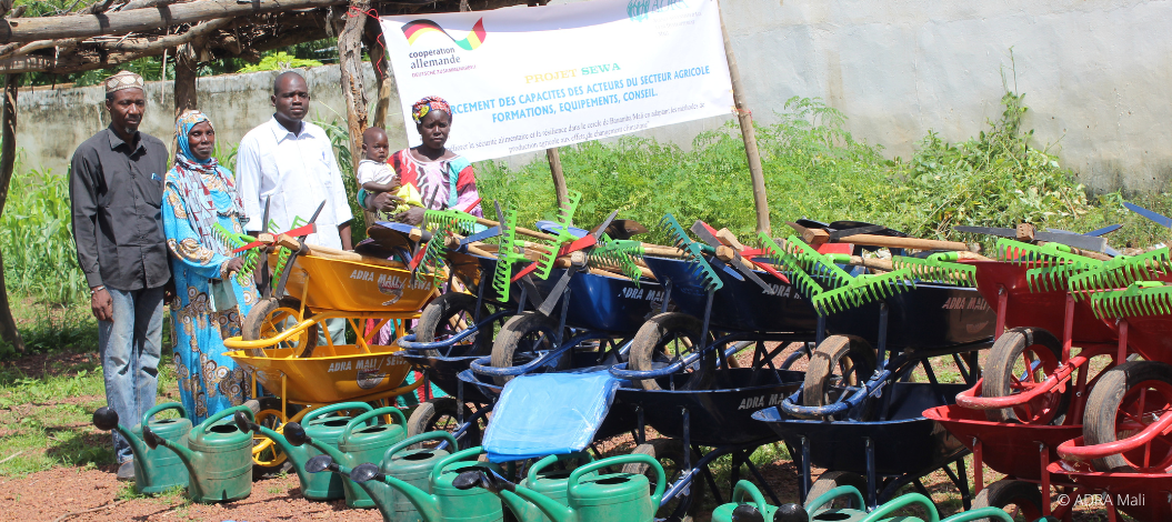Vier Erwachsene und ein Kleinkind betrachten draußen eine Auswahl an Gartenwerkzeugen