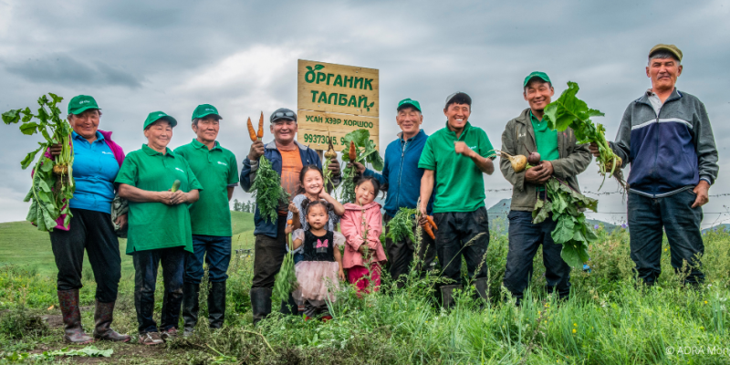 Biolandwirte und drei Kleinkinder aus der Mongolei stehen im Feld und halten das geernte Gemüse in den Händen.