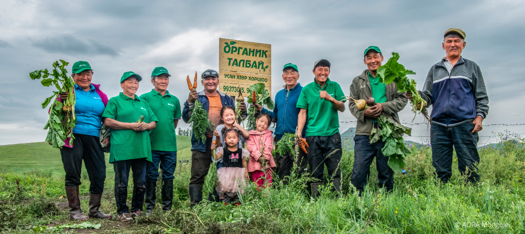 Biolandwirte und drei Kleinkinder aus der Mongolei stehen im Feld und halten das geernte Gemüse in den Händen.
