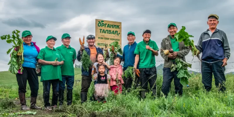 Biolandwirte und drei Kleinkinder aus der Mongolei stehen im Feld und halten das geernte Gemüse in den Händen.