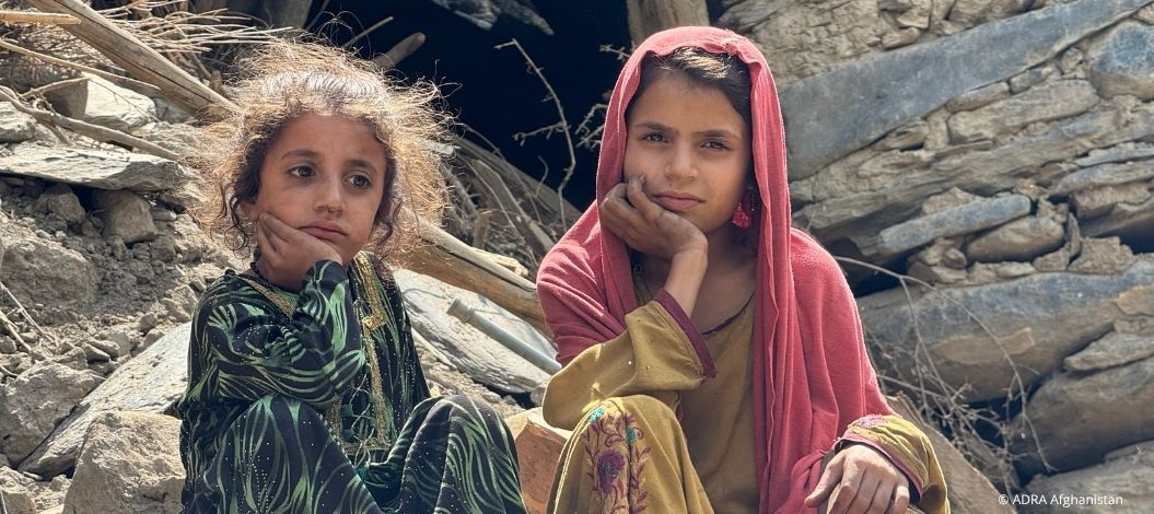 Zwei Mädchen sitzen nach dem Erdbeben 2025 vor zerstörten Häusern in Afghanistan.