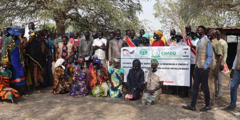 Über 20 Menschen im Südsudan stehen im Freien und präsentieren mit einem Schild ein ADRA-Projekt