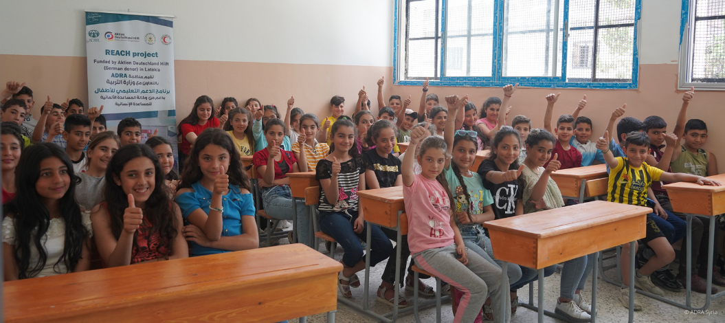 Eine gemischt Schulklasse sitzt in einem Klassenzimmer. Alle Kinder strecken die Hände nach oben und strahlen Freude aus.