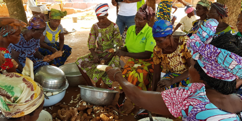Eine Gruppe Frauen in togolesischer Kleidung sitzt auf dem Boden und bereitet Essen vor