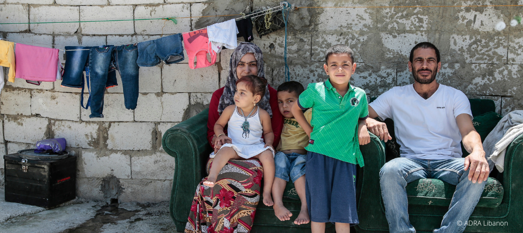 Eine libanesische Familie mit drei Kindern sitzt im Freien auf einem Sofa, während bunte Wäsche auf der Wäscheleine im Hintergrund hängt
