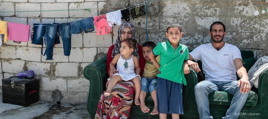 Libanesische Familie mit drei Kindern sitzt draußen auf Sofa, bunte Wäsche hängt im Hintergrund