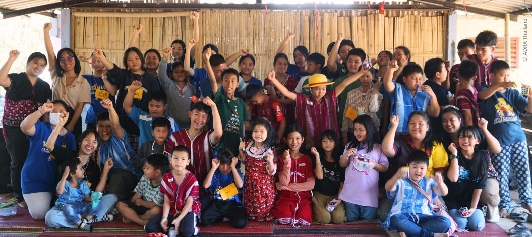 Gruppe von Kindern und Erwachsenen in traditioneller Kleidung posiert lachend mit erhobenen Fäusten bei ADRA-Thailand-Aktion