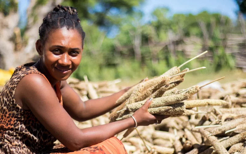 Eine Frau hält das Hirsegetreide in beiden Händen, neben ihr liegt noch weitere Ernte von der Hirse