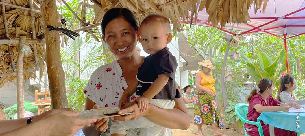 Myanmar_Header_Nothilfe_nach_erdbeben Frau mit Jungen auf dem Arm erhält Umschlag mit Geld.