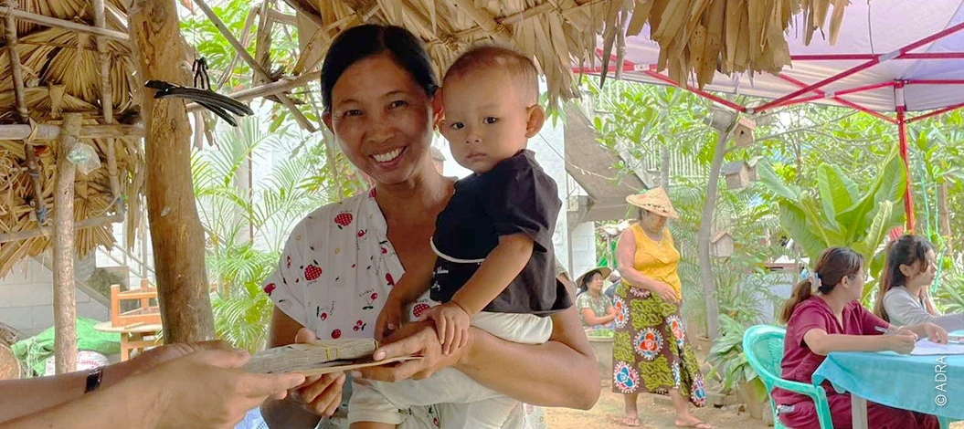 Frau mit Jungen auf dem Arm erhält Umschlag mit Geld.