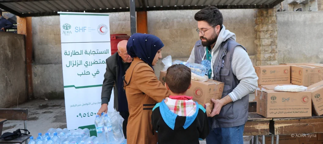 Nach Erdbeben in Nordsyrien: ADRA-Mitarbeiter übergibt Nothilfe-Pakete an Frau mit Kind, Mann hält Wasserflaschen
