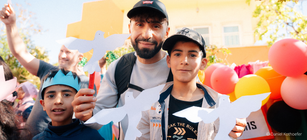 Rapper MoTrip steht im Schulhof einer Schule im Libanon mit Kindern und halten gemeinsam weißen Papiertauben in den Händen.
