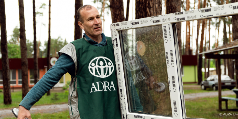 Ein ADRA- Mitarbeiter in grüner ADRA-Weste trägt ein neues Fenster