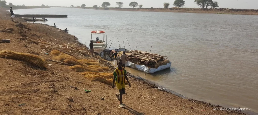 Ein Junge läuft am Ufer eines Flusses, dahinter ist ein Floss, mit dem Baumstämme und Holz transportiert werden