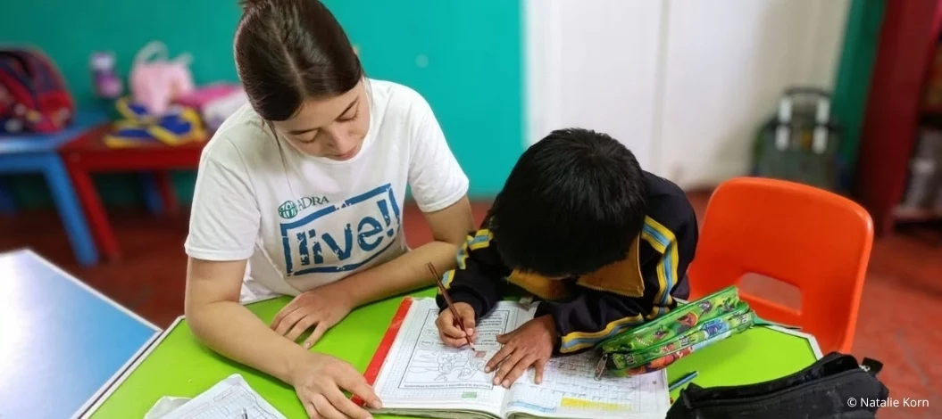 Junge ADRAlive!-Freiwillige unterstützt ein Schulkind beim Lernen in einem Klassenraum im Globalen Süden