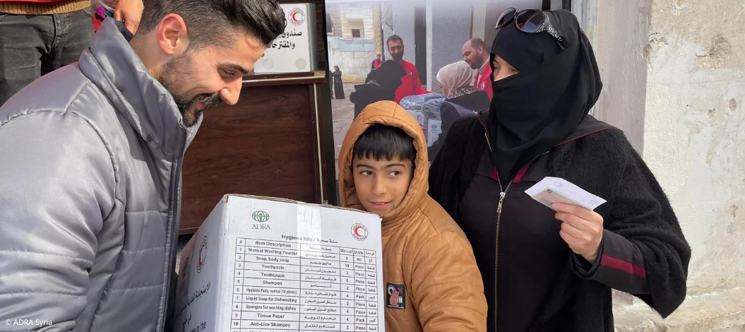 ADRA-Mitarbeiter übergibt nach dem Erdbeben in Aleppo einem Jungen und seiner Mutter ein Hilfspaket