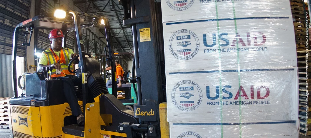 Ein Gabelstaplerfahrer transportiert Hilfsgüter mit dem USAID-Logo in einem Lagerhaus.