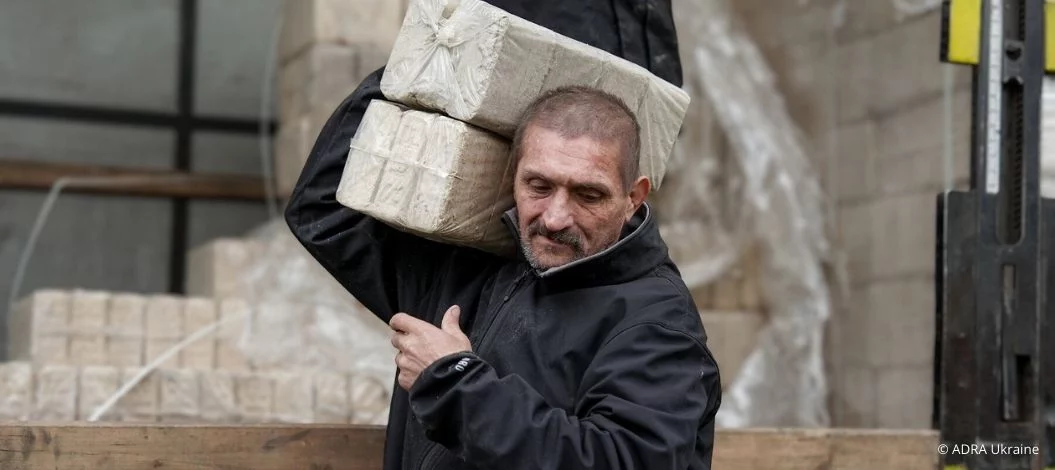 Ein Mann trägt gepresste Brennstoffblöcke von einem Lkw, die im Rahmen der ADRA-Winterhilfe in der Ukraine verteilt werden.
