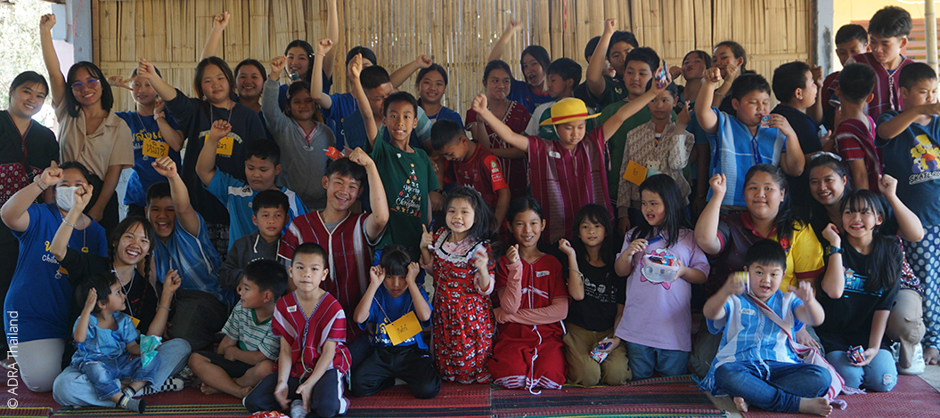 Gruppe von Kindern und Erwachsenen in traditioneller Kleidung posiert lachend mit erhobenen Fäusten bei ADRA-Thailand-Aktion