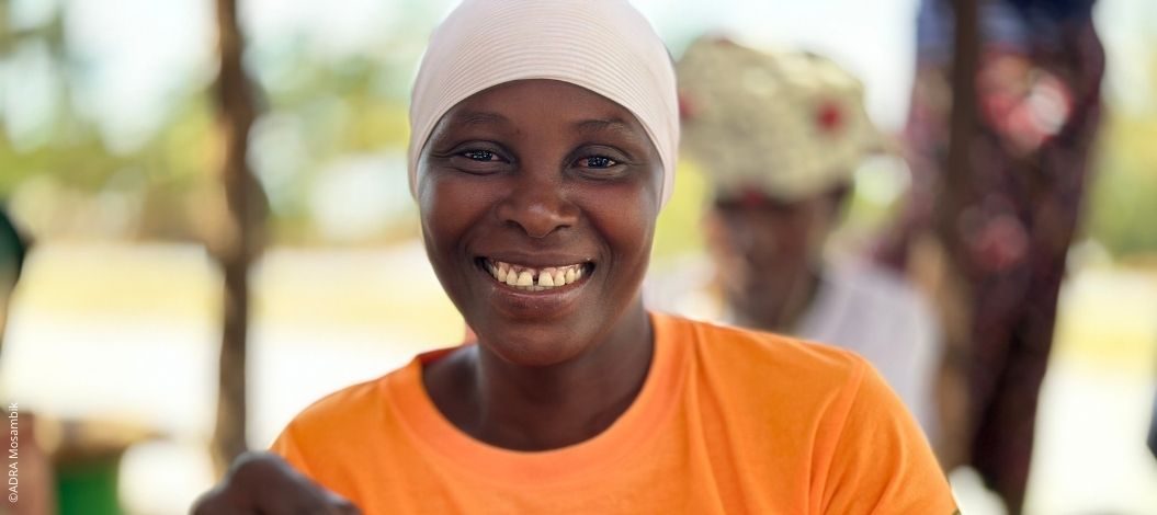 Lächelnde Frau aus Mosambik mit orangefarbenem T-Shirt blickt direkt in die Kamera.