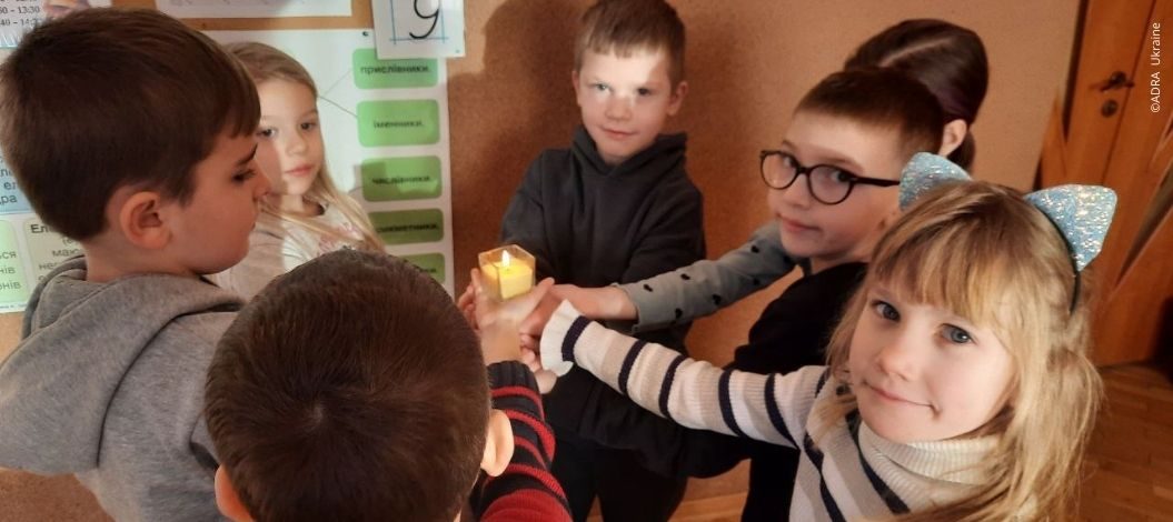 Sieben Kinder in der Ukraine halten gemeinsam eine brennende Kerze – Symbol für Hoffnung und Gemeinschaft im ADRA-Bildungsprojekt